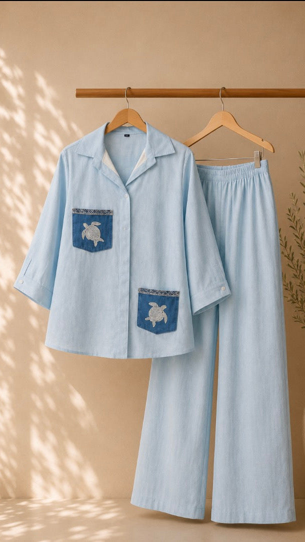 Light blue pajama set with turtle design on hangers against a beige wall.